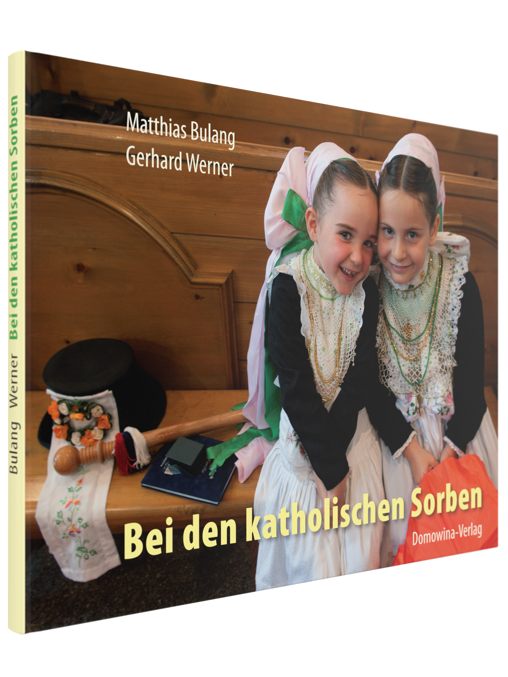 "Buchcover von 'Bei den katholischen Sorben' von Matthias Bulang und Gerhard Werner, erschienen im Domowina-Verlag. Das Cover zeigt zwei junge Mädchen in traditioneller sorbischer Tracht mit weißen Spitzenkragen, Perlenketten und großen Schleifen im Haar.